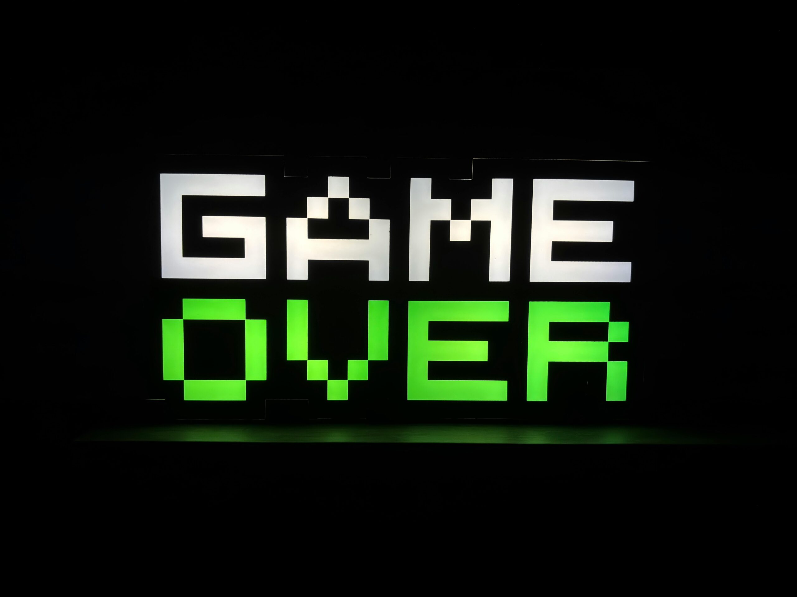 Illuminated 'Game Over' sign in pixel art style with neon green and white colors on a dark background.